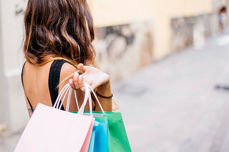 Una chica con un estilo actual parece haber buscado “influencers moda instagram” para empaparse de las tendencias antes de ir de compras, se la ve con tres bolsas de tiendas de ropa en las manos. 