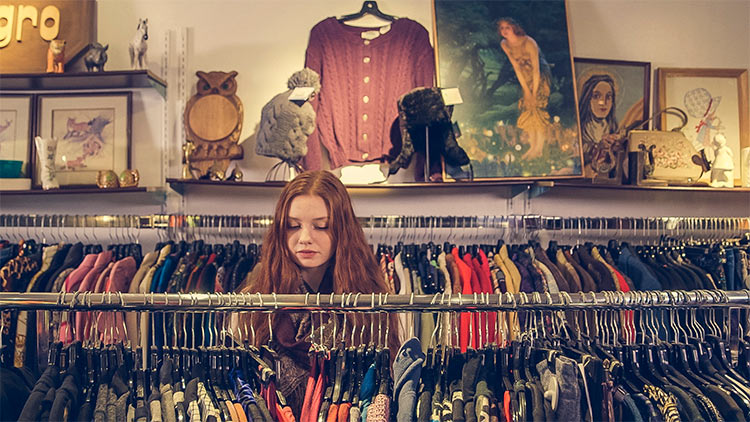 En medio de una tienda de ropa, una chica joven pelirroja mirando las prendas aparentemente tranquila.