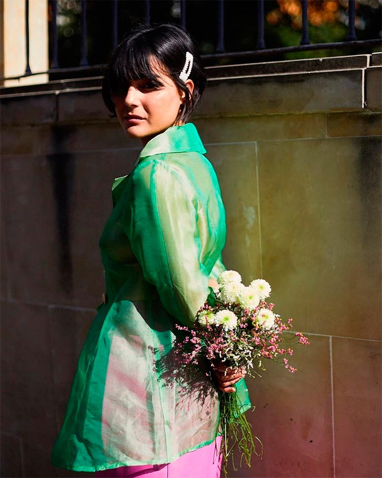 La influencer María Bernad posando con una falda y una camisa larga vintage de su propia marca, con un ramo de flores en la mano