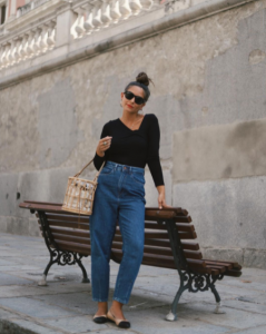 La influencer Erea Louro poda junto aun banco con unos pantalones vaqueros de mujer, un bolso beige y una camiseta negra